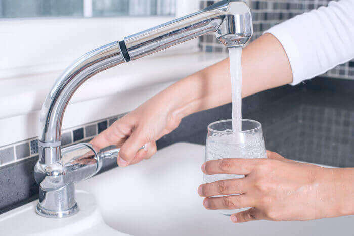 A woman filling a cup of water at the kitchen sink