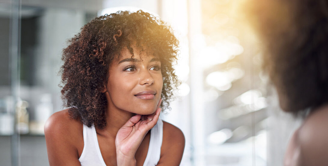 A woman staring at herself in the mirror with her hand on her chin.