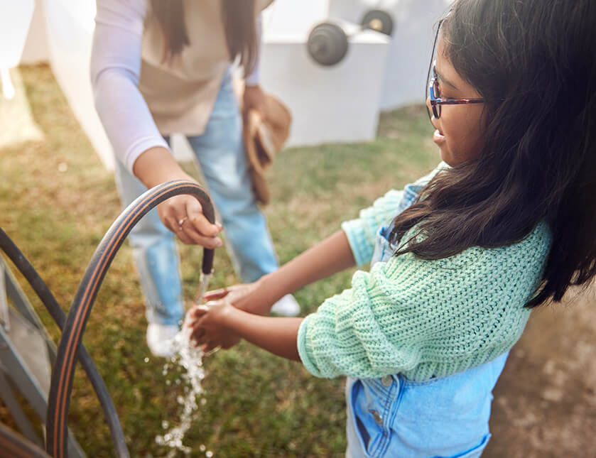 A young girl with her hand under a water hose.