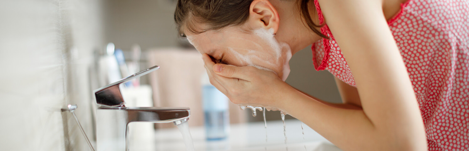 A woman washing her face in the bathroom sink