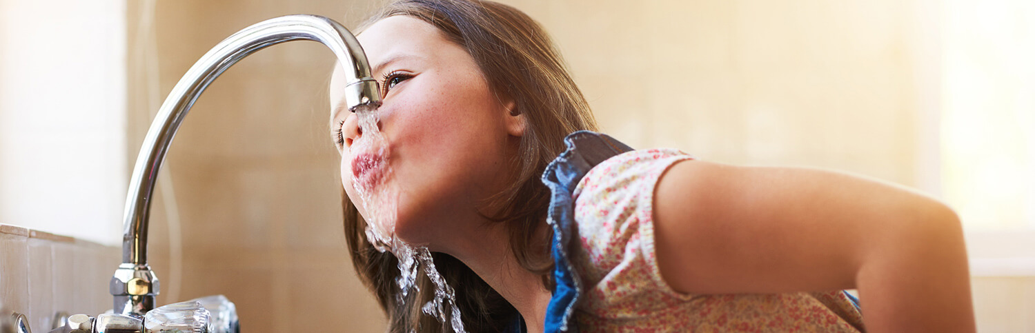 A young girl drinking water out of a kitchen sink