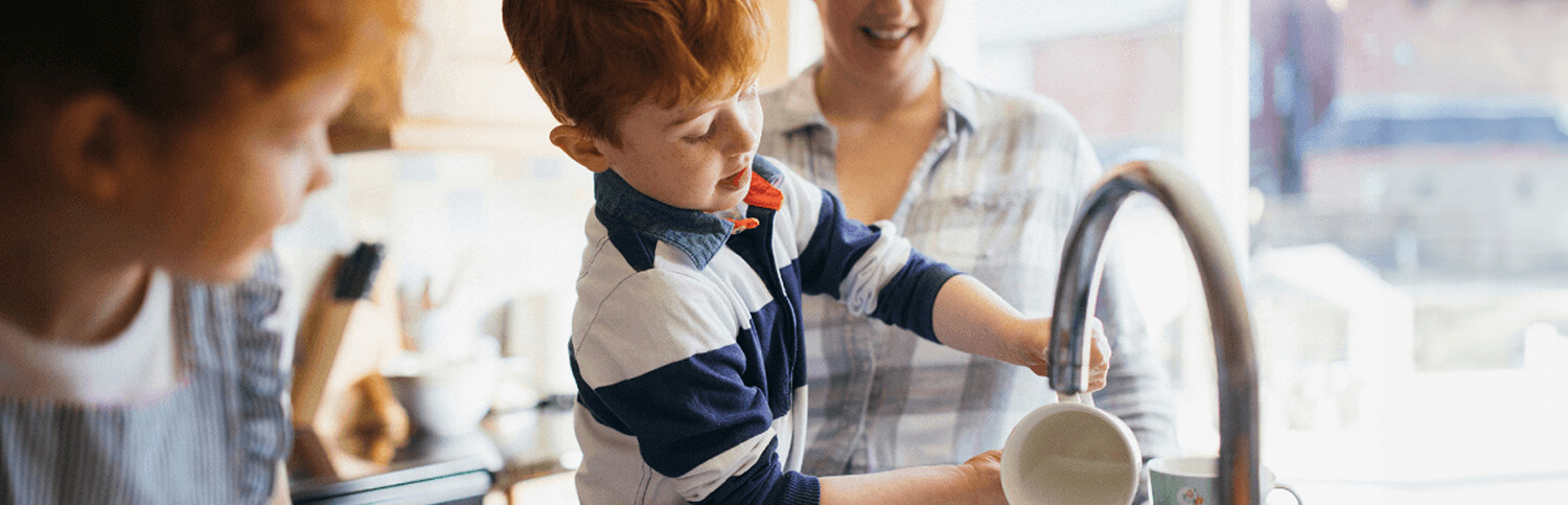 A young boy washing a mug at a kitchen sink